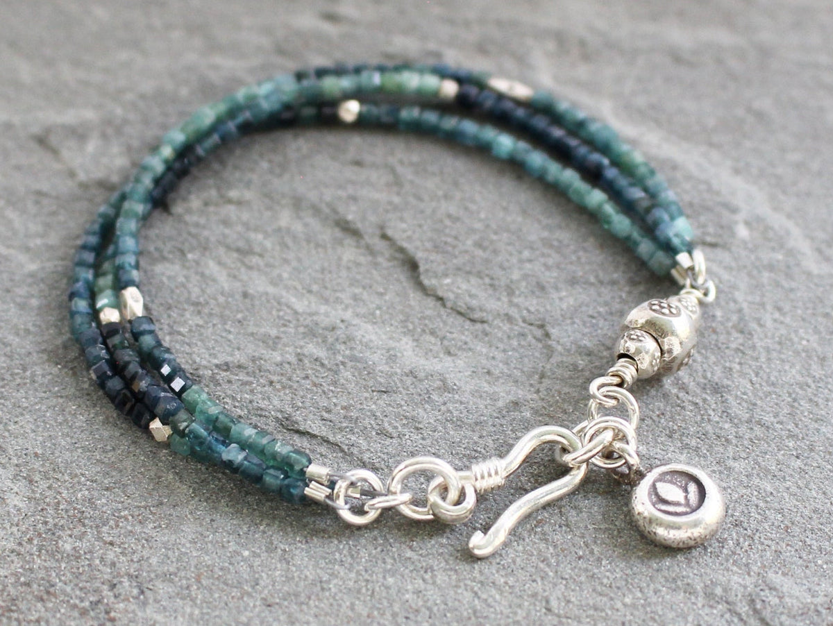 Triple strand beaded bracelet with ombre blue and teal tourmaline cubes, accented by small silver spacer beads and a silver hook clasp with a lotus charm.