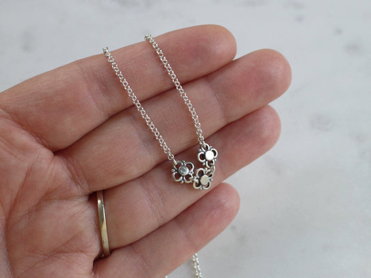 Silver necklace with a floral pendant held in a hand against a marble background