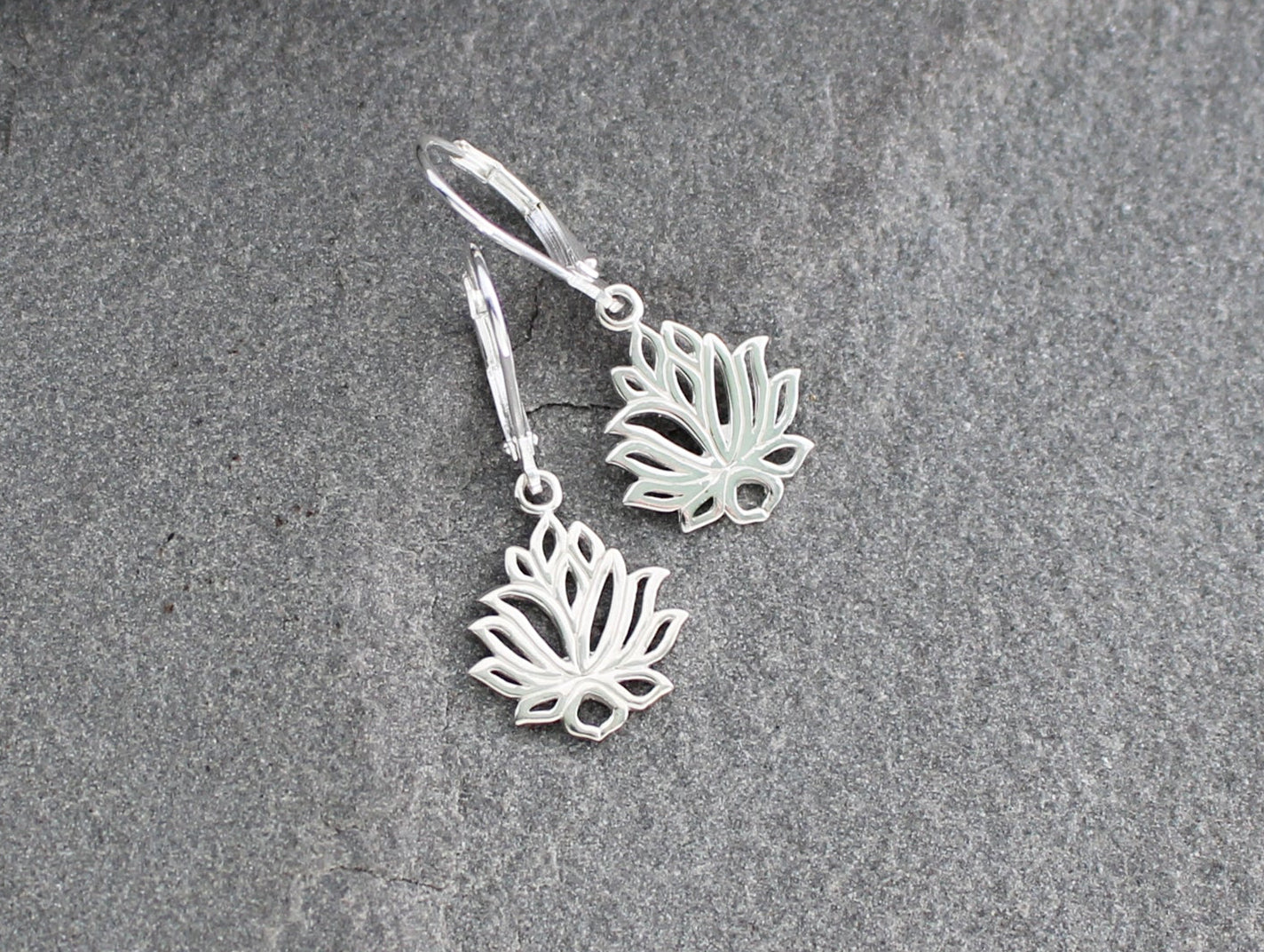 Silver lotus flower earrings on a textured stone surface