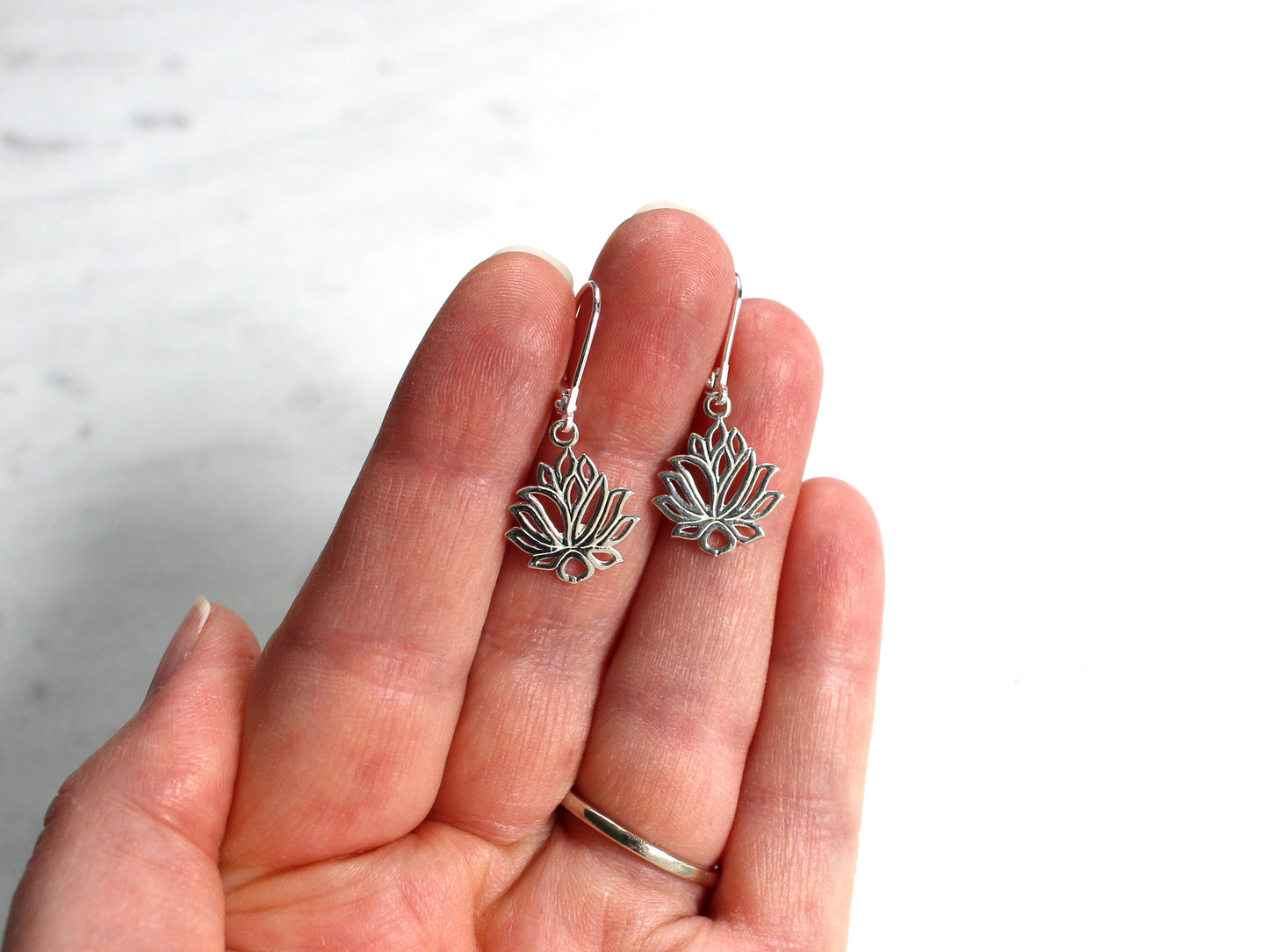 Silver lotus flower earrings held in a hand against a white background