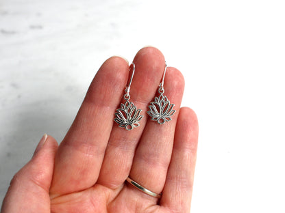 Silver lotus flower earrings held in a hand against a white background