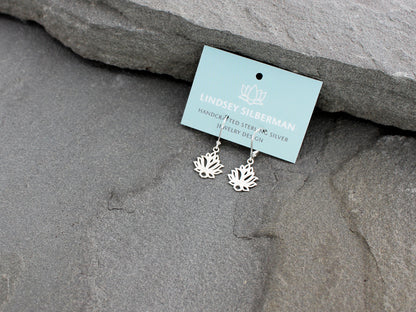 Silver lotus flower earrings on a card with 'Lindsey Silberman' branding, placed on gray stone.