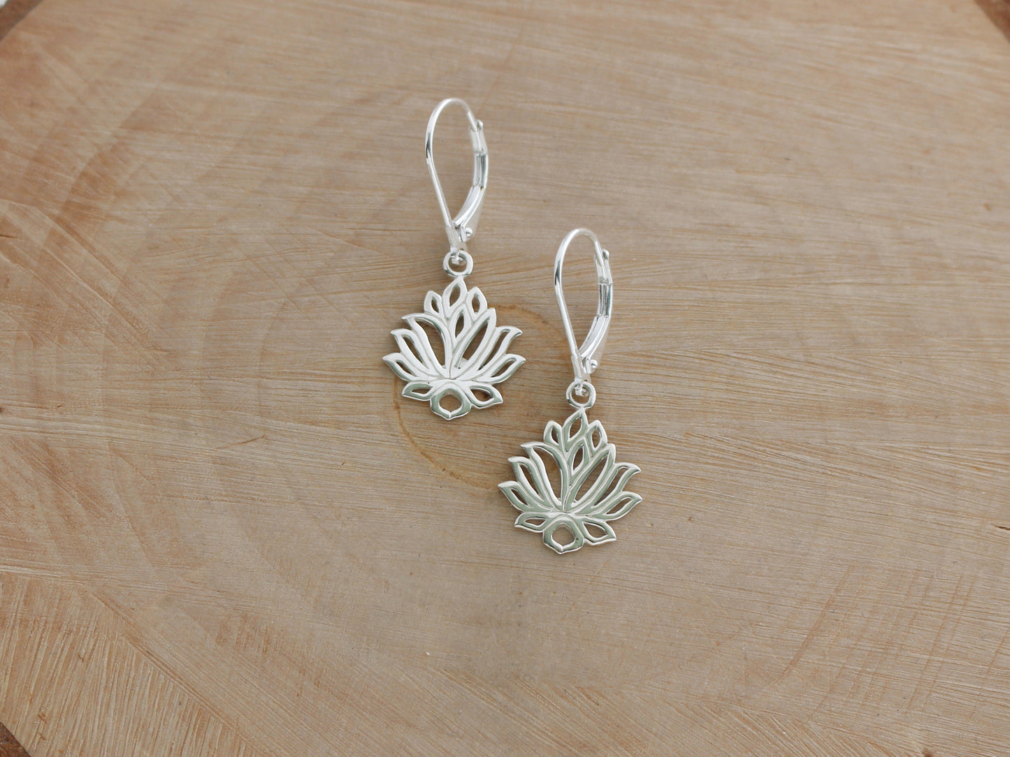 Silver lotus flower earrings on a wooden surface