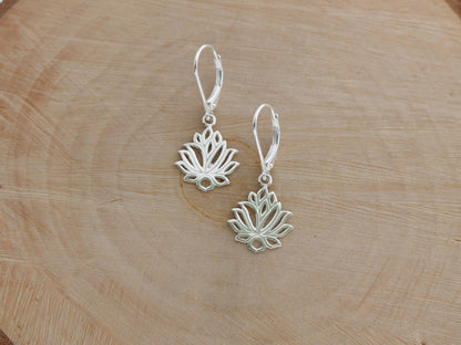 Silver lotus flower earrings on a wooden surface