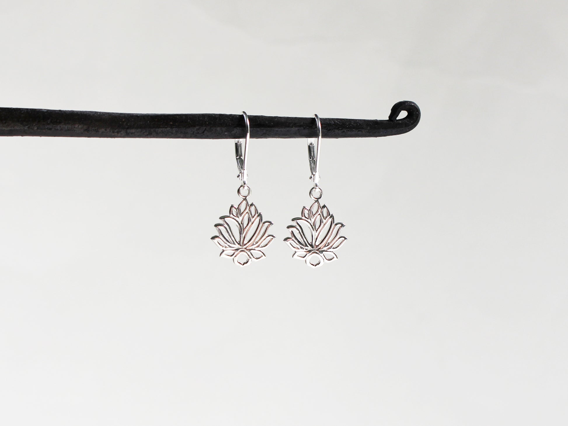 Silver lotus flower earrings on a black hook against a white background