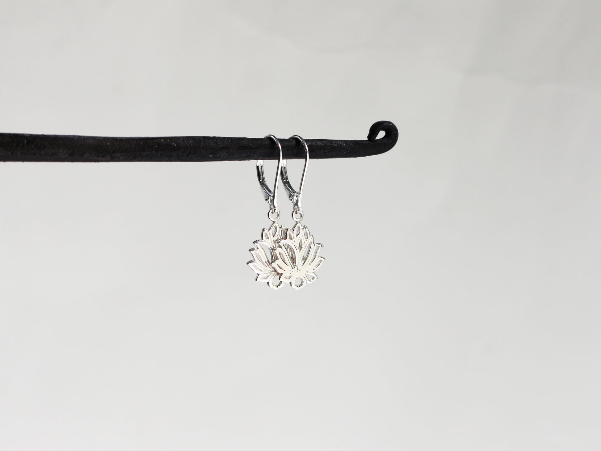 Silver lotus flower earrings on a black hook against a light gray background