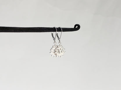Silver lotus flower earrings on a black hook against a light gray background