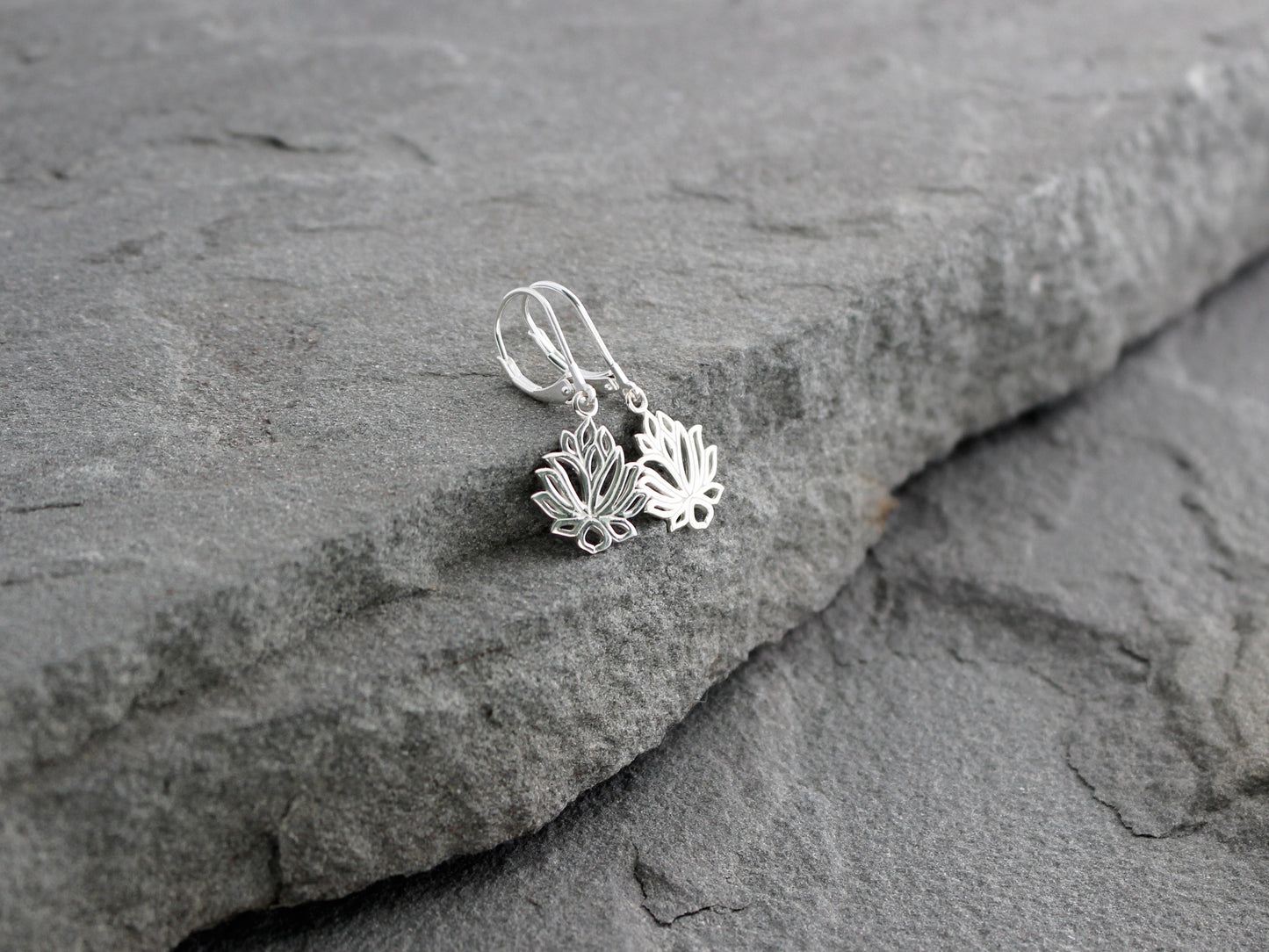 Silver lotus flower earrings on a stone surface