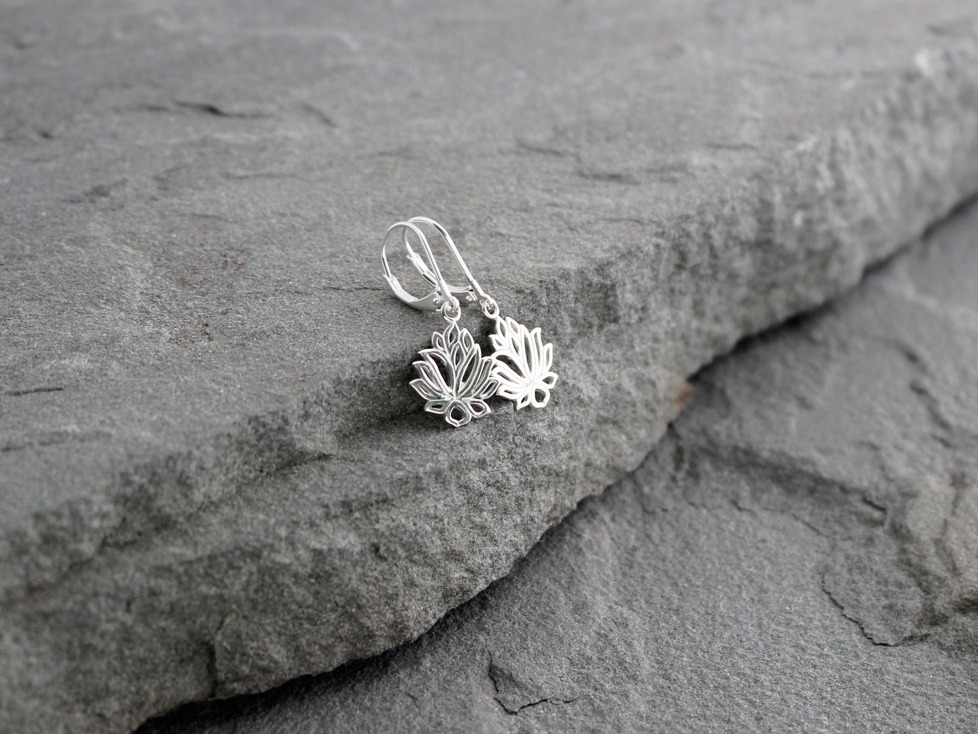 Silver lotus flower earrings on a stone surface