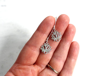 Silver lotus flower earrings held in a hand against a white background